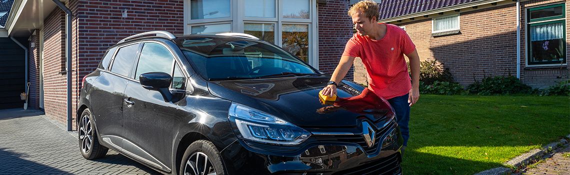 man poetst auto voor zijn woning