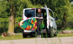vrouw met supboard staat achter haar verzekerde bestelauto langs rivier