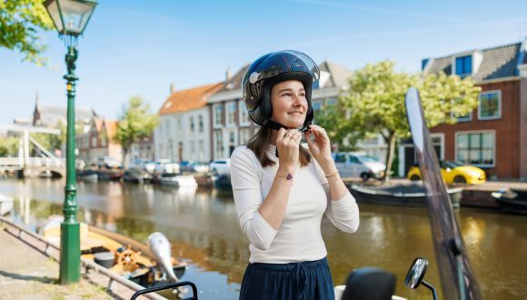 Vrouw aan gracht doet helm op voordat ze op de bromfiets stapt