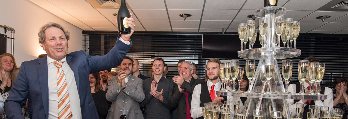 Man met champagnefles, toren van champagneglazen en klappende mensen op de achtergrond