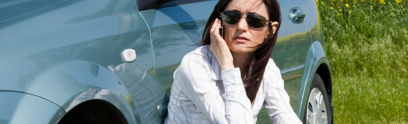 vrouw met pech zit tegen haar auto aan te telefoneren